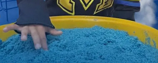 Mano de un niño pequeño explorando arena azul en una tina amarilla