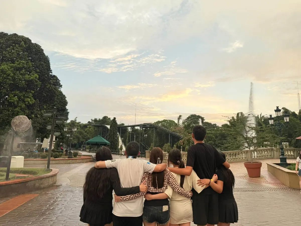 Grupo de estudiantes abrazados, de espaldas, frente a un parque al atardecer